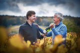 Father and son in a vineyard gifting a bottle of champagne.