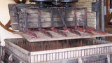 Vintage wooden press with metal components, featuring a date stamp, against a colorful mural background.